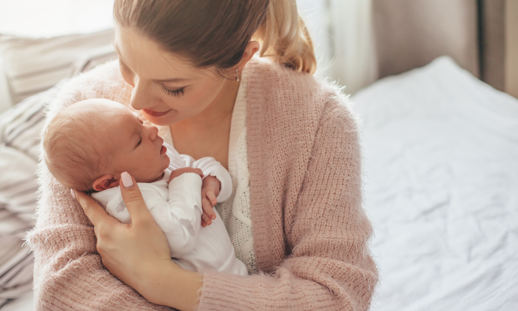 mom holding an infant and sitting on a bed