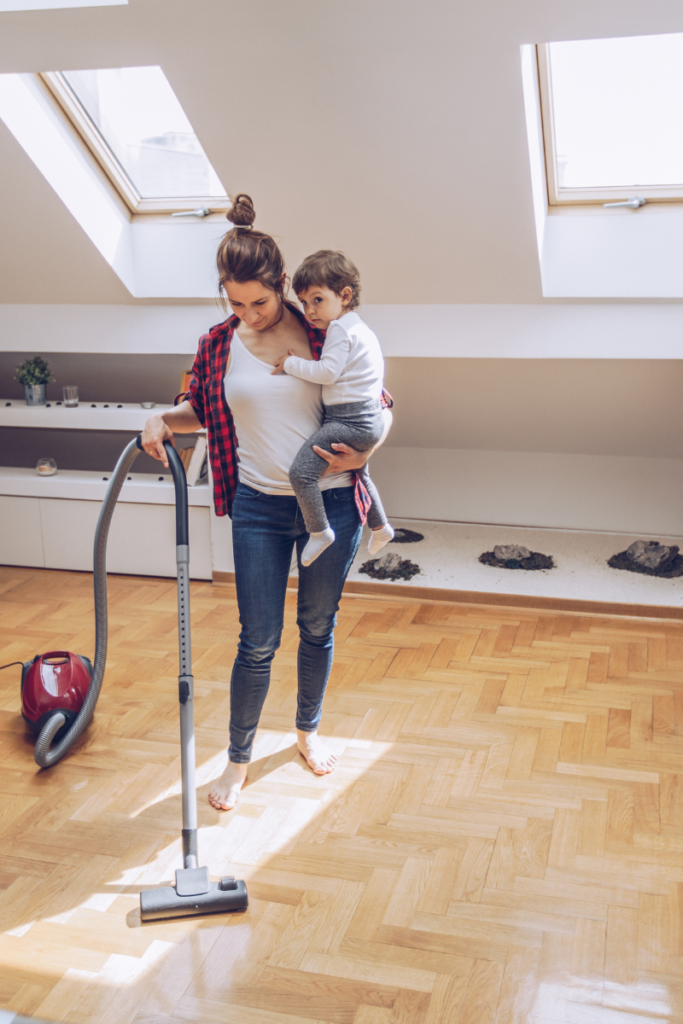 mom holding a little boy vacuuming a hard wood floor