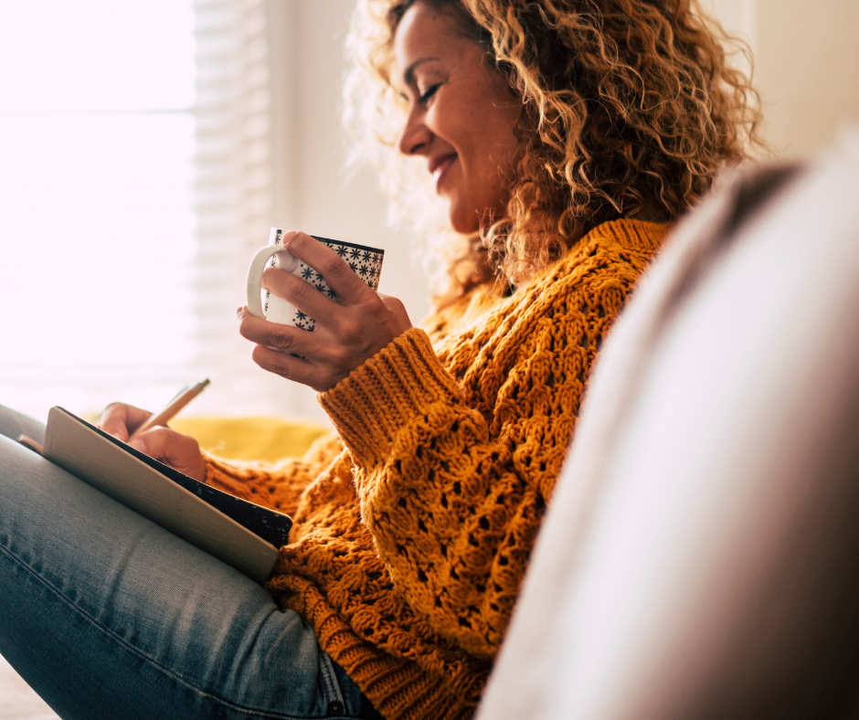 woman holding a mug of coffee writing in a notebook - what it really means to be happy