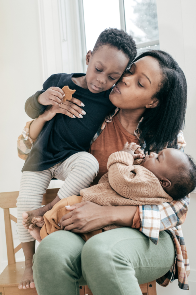 mom holding a baby in one arm and a toddler in another arm sitting on a chair