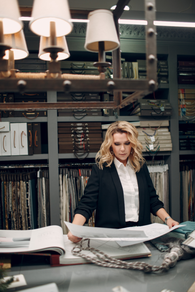 a woman wearing a black blazer and a white shirt holding large papers in front of her at work 