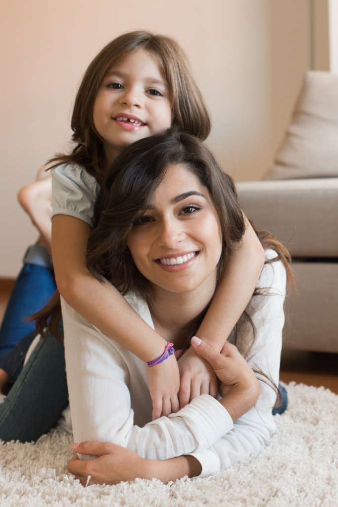 Mom and daughter laying on the floor of the living room smiling into the camera - embracing change