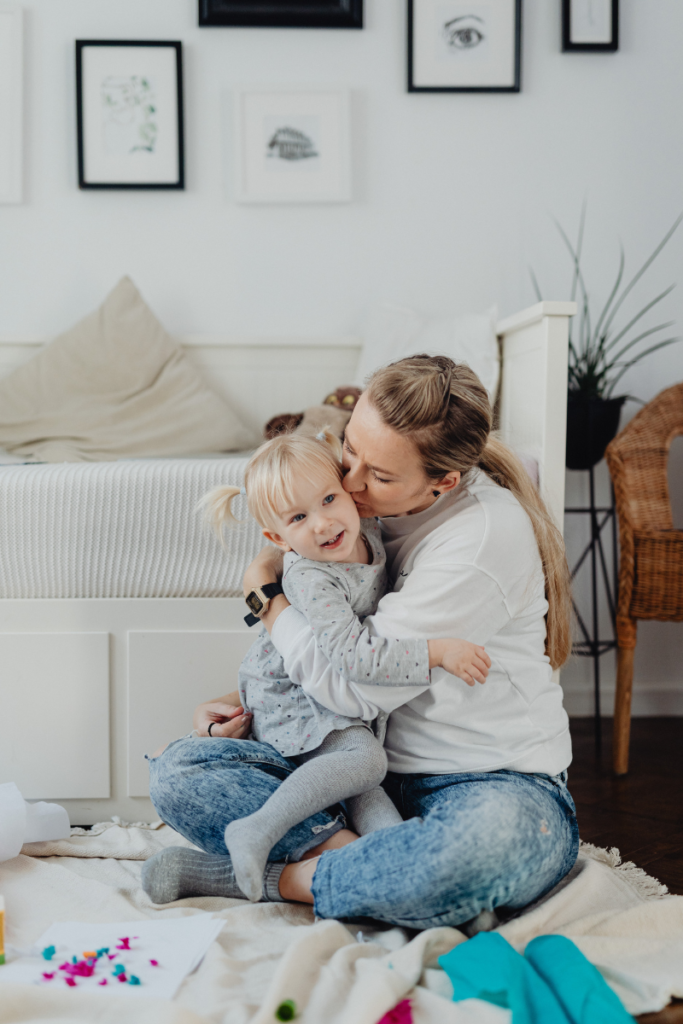 Mom Guilt - A mom kissing her daughter on the cheek sitting on the floor of the living room