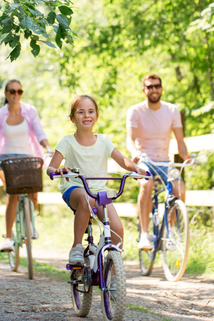 girl riding a bike in front of her parents on a tree lined dirt road - summer time fun