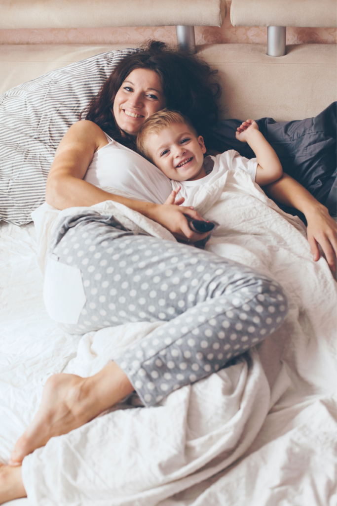 nurturing relationships - a mom and child laying in bed together wearing pajamas and smiling at the camera