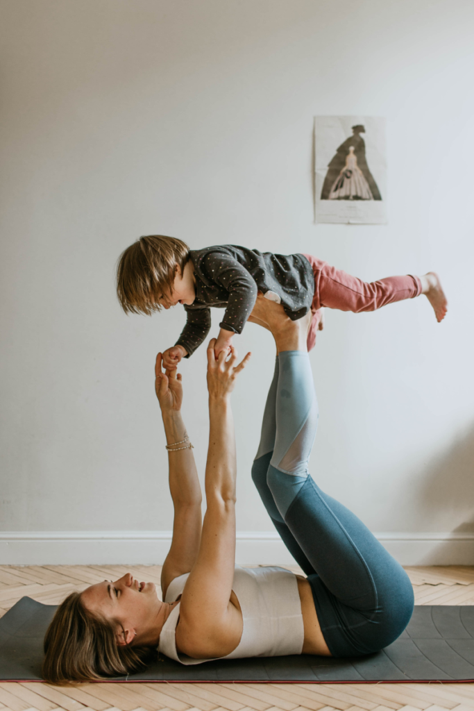 Woman in yoga pants laying on the floor holding a little boy up in the air on her feet