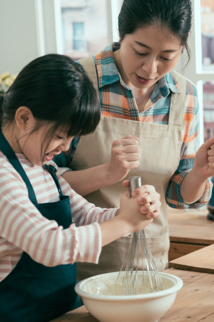 mom and girl in a kitchen wearing aprons whisking in a bowl