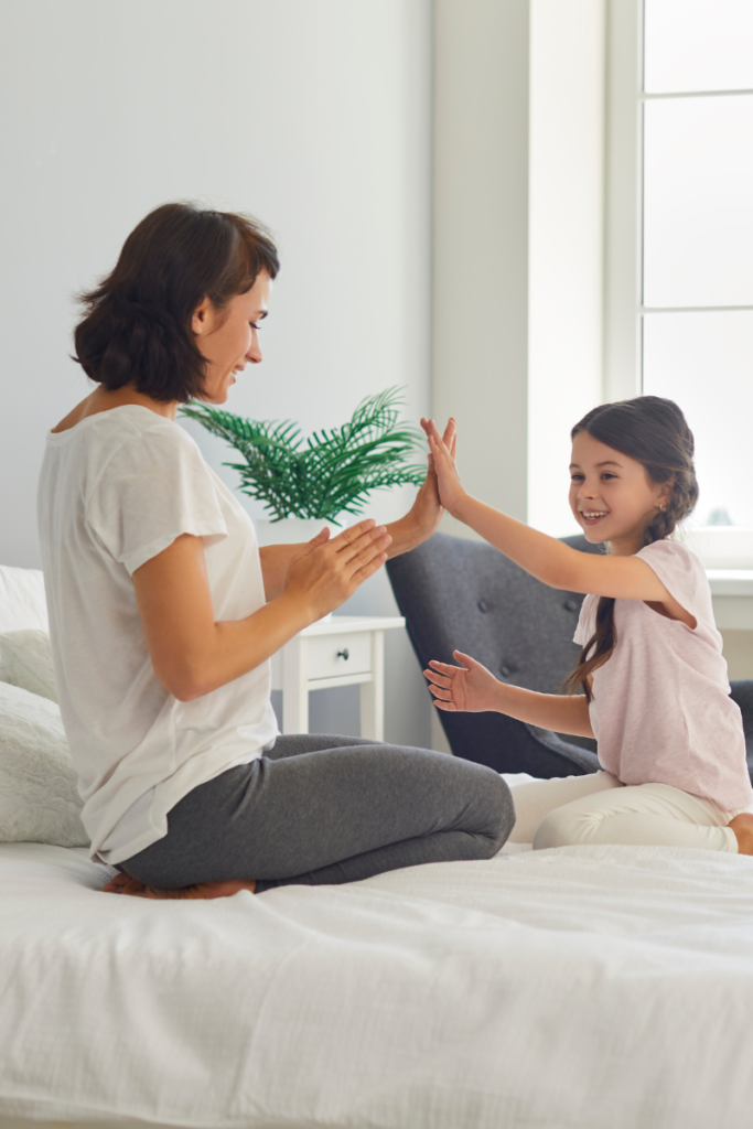 woman and little girl high fiving on a white bed