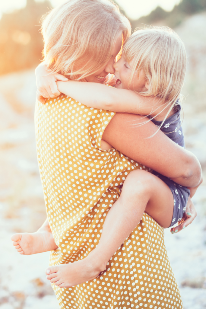 woman holding a child at the beach with the setting sun in the background