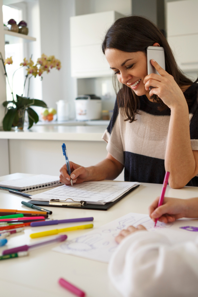 woman holding a phone and writing on a piece of paper at the kitchen table