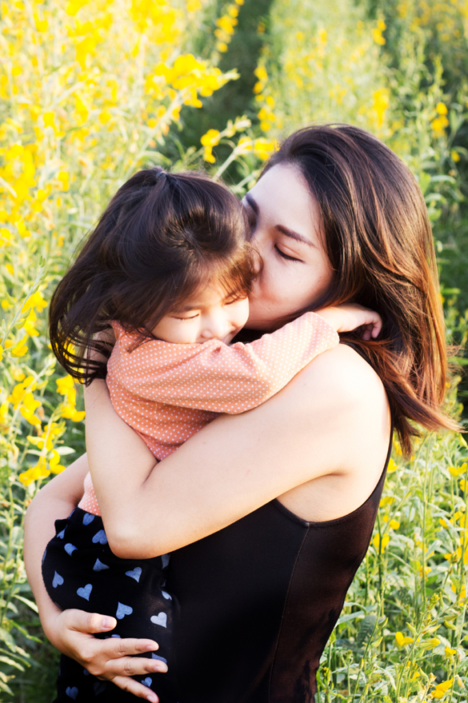 mom holding daughter kissing her cheek in a field of flowers