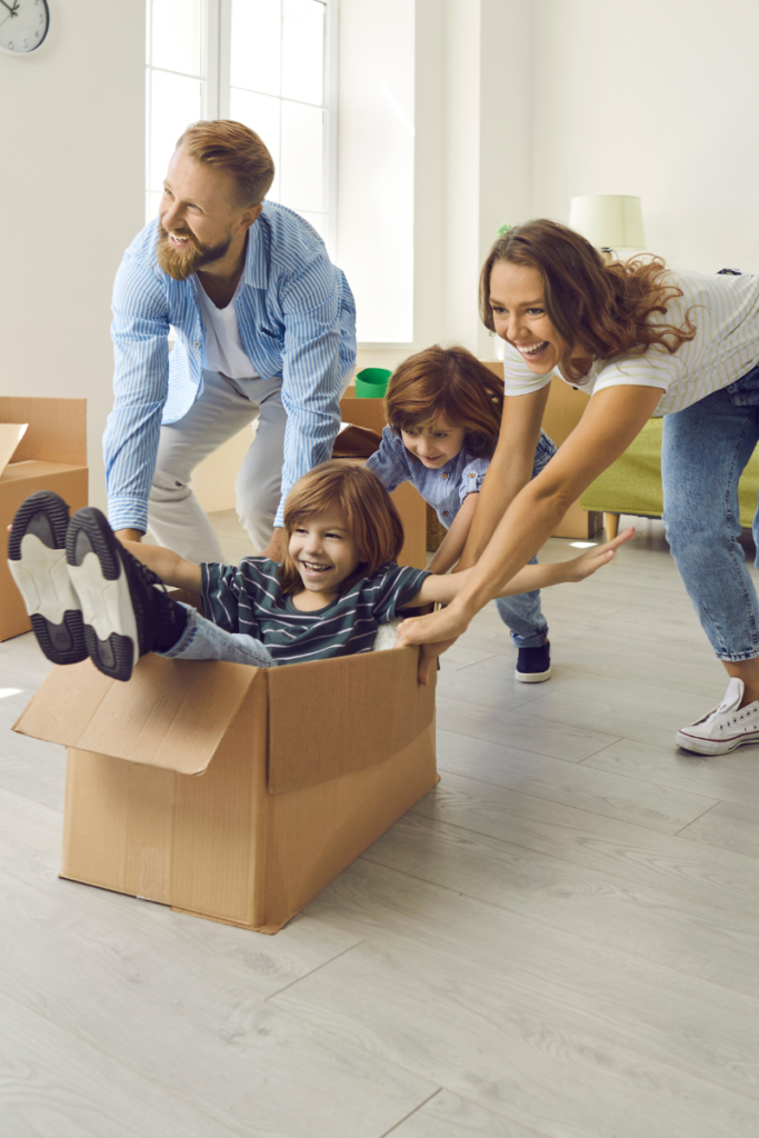 mom, dad, and kid pushing a boy in a box on a hard wood floor